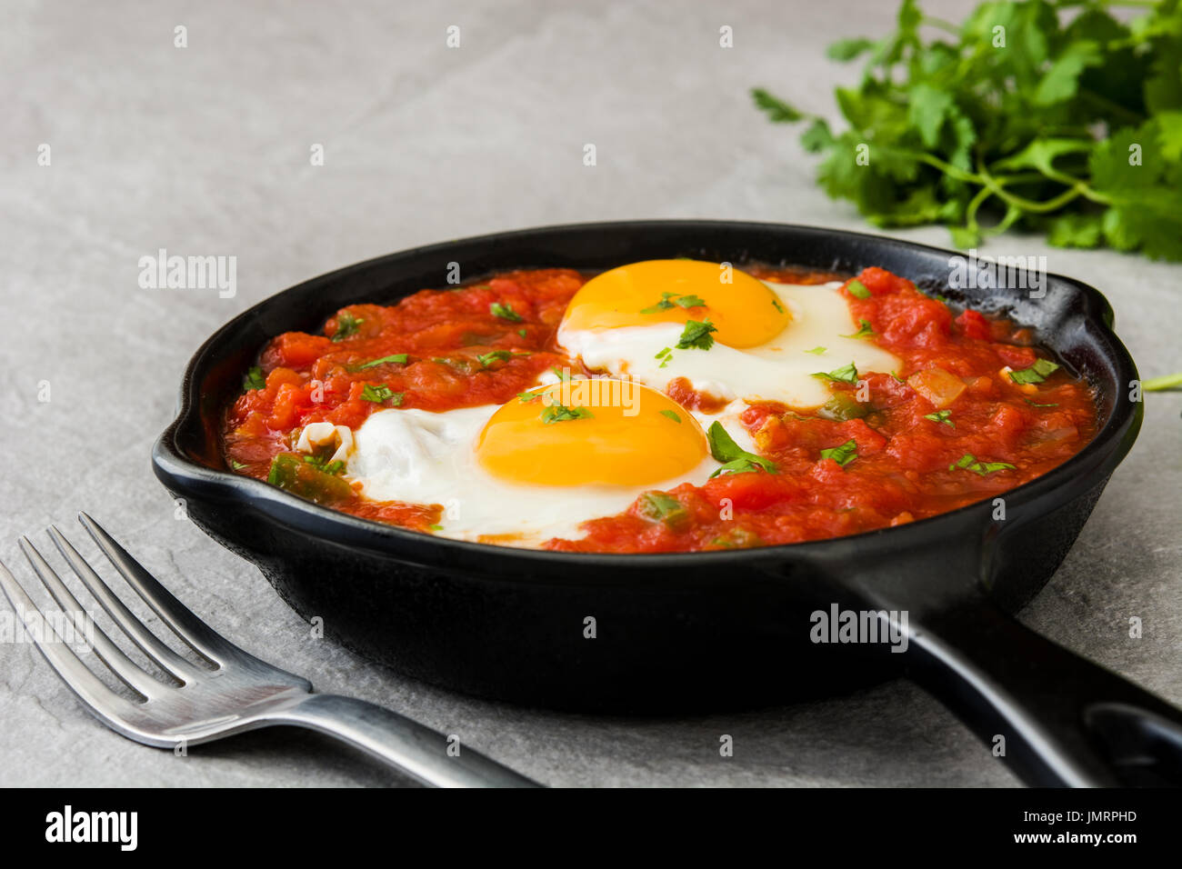 Mexican breakfast: Huevos rancheros in iron frying pan on gray stone Stock Photo