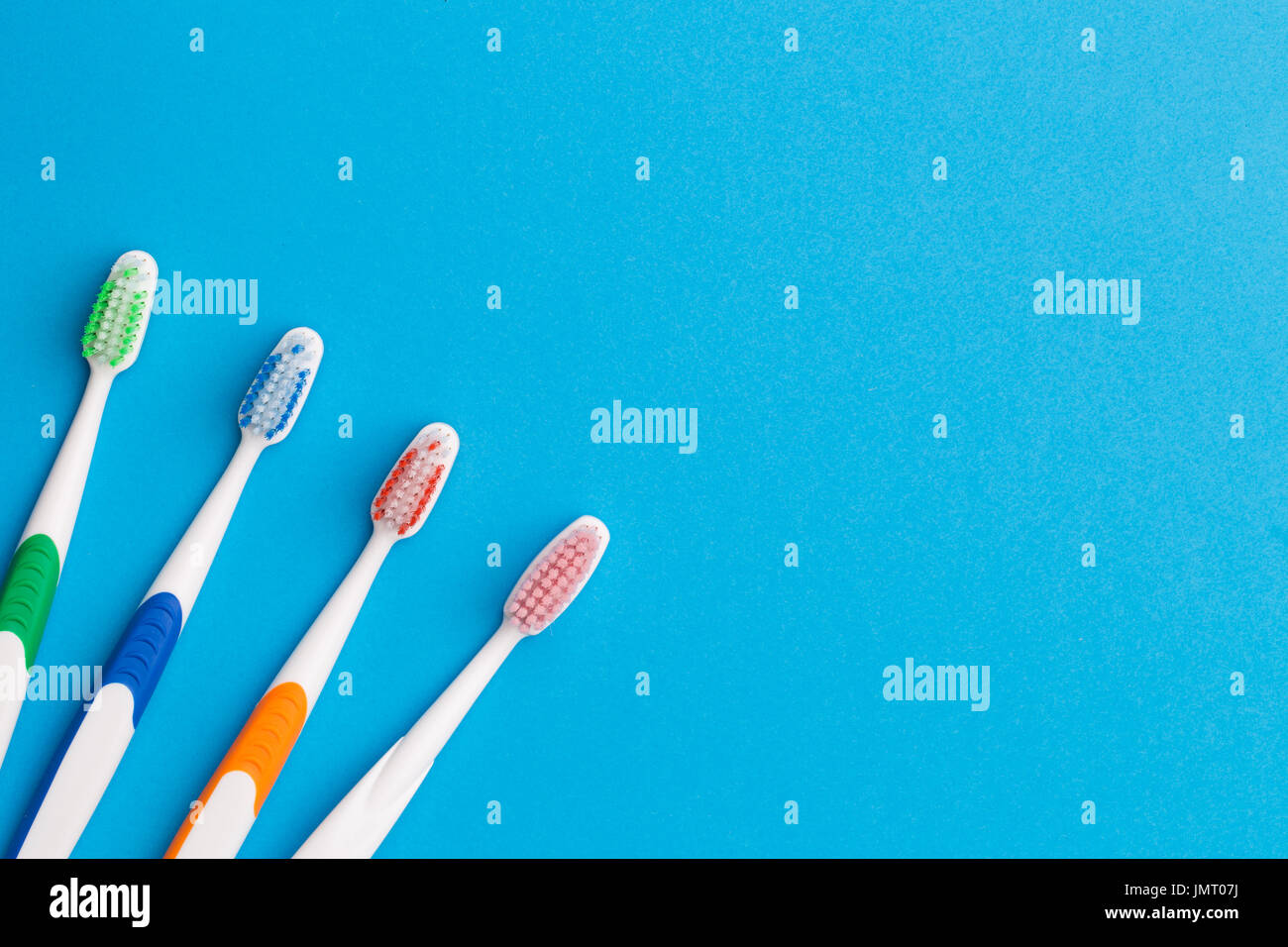 Four multicolored toothbrushes on empty blue background, place for words Stock Photo