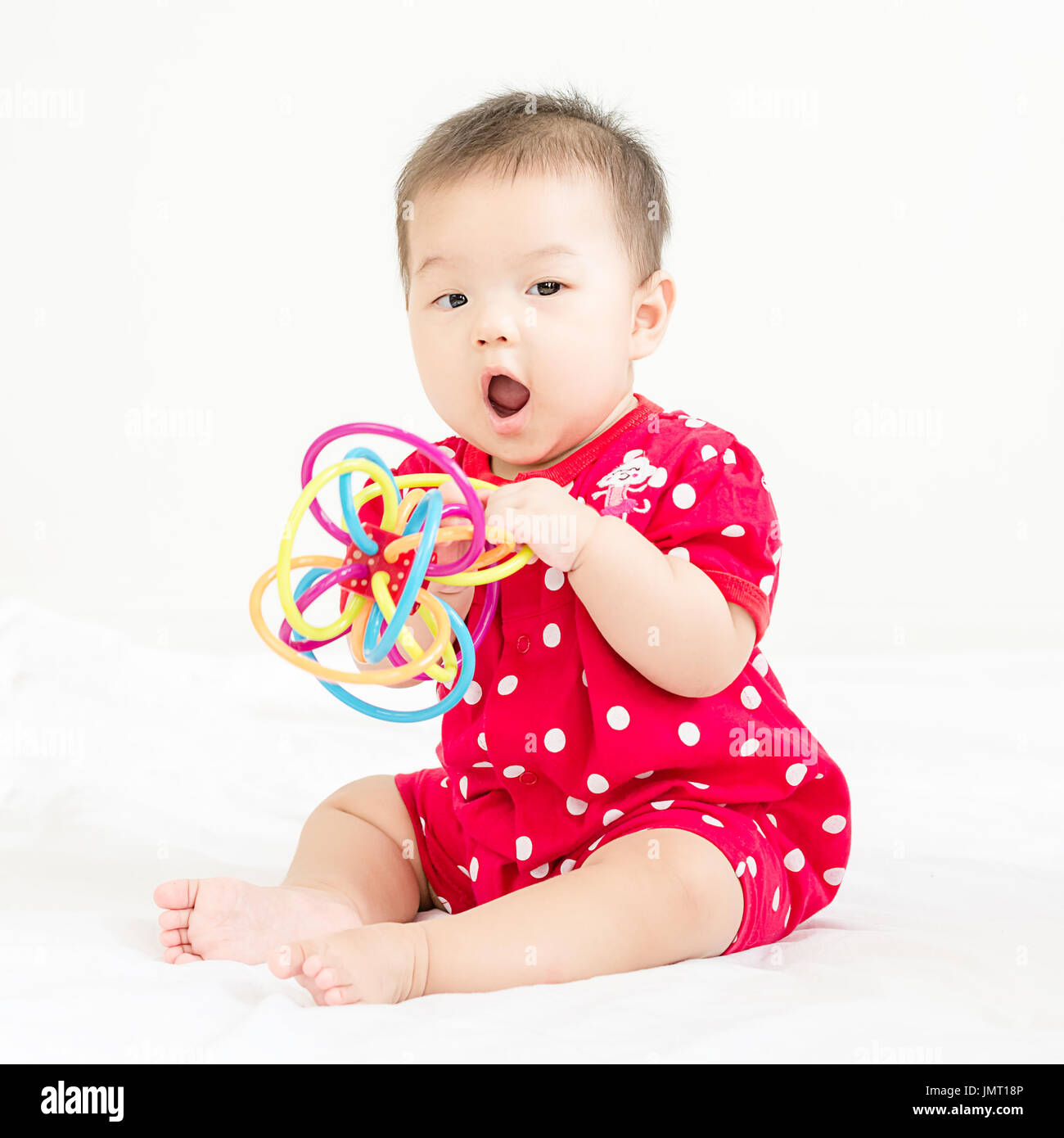 Portrait of a little adorable infant baby girl sitting on the bed and smiling to camera with bites toy Stock Photo