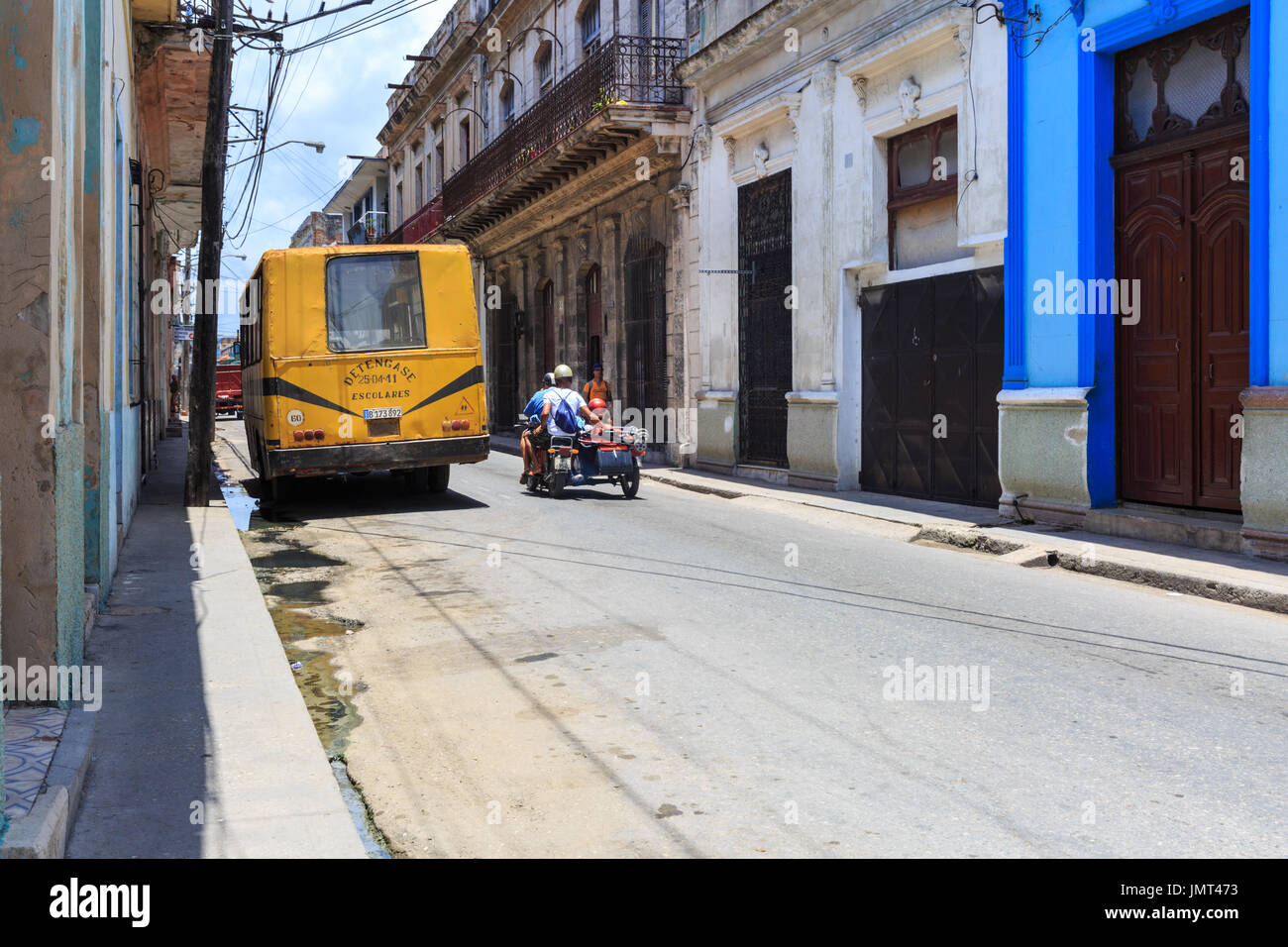 Street scene with vintage school bus and people on motorcycle in Matanzas, Cuba Stock Photo