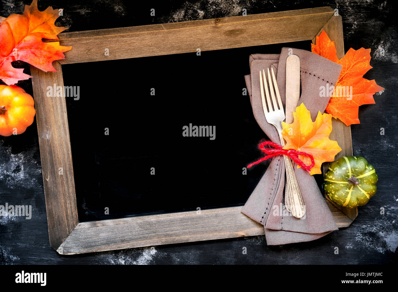 Autumn menu concept - rustic table place setting with a fork and a knife wrapped in a napkin with fall season decorative leaves and pumpkins with chal Stock Photo
