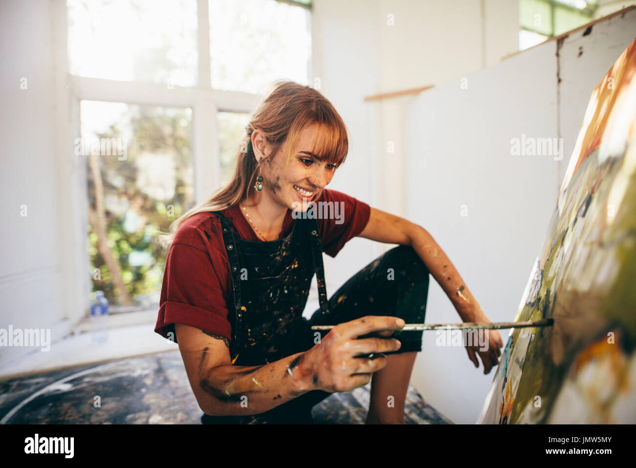 Indoor shot of professional female artist painting on canvas in studio. Woman painter painting in her workshop. Stock Photo