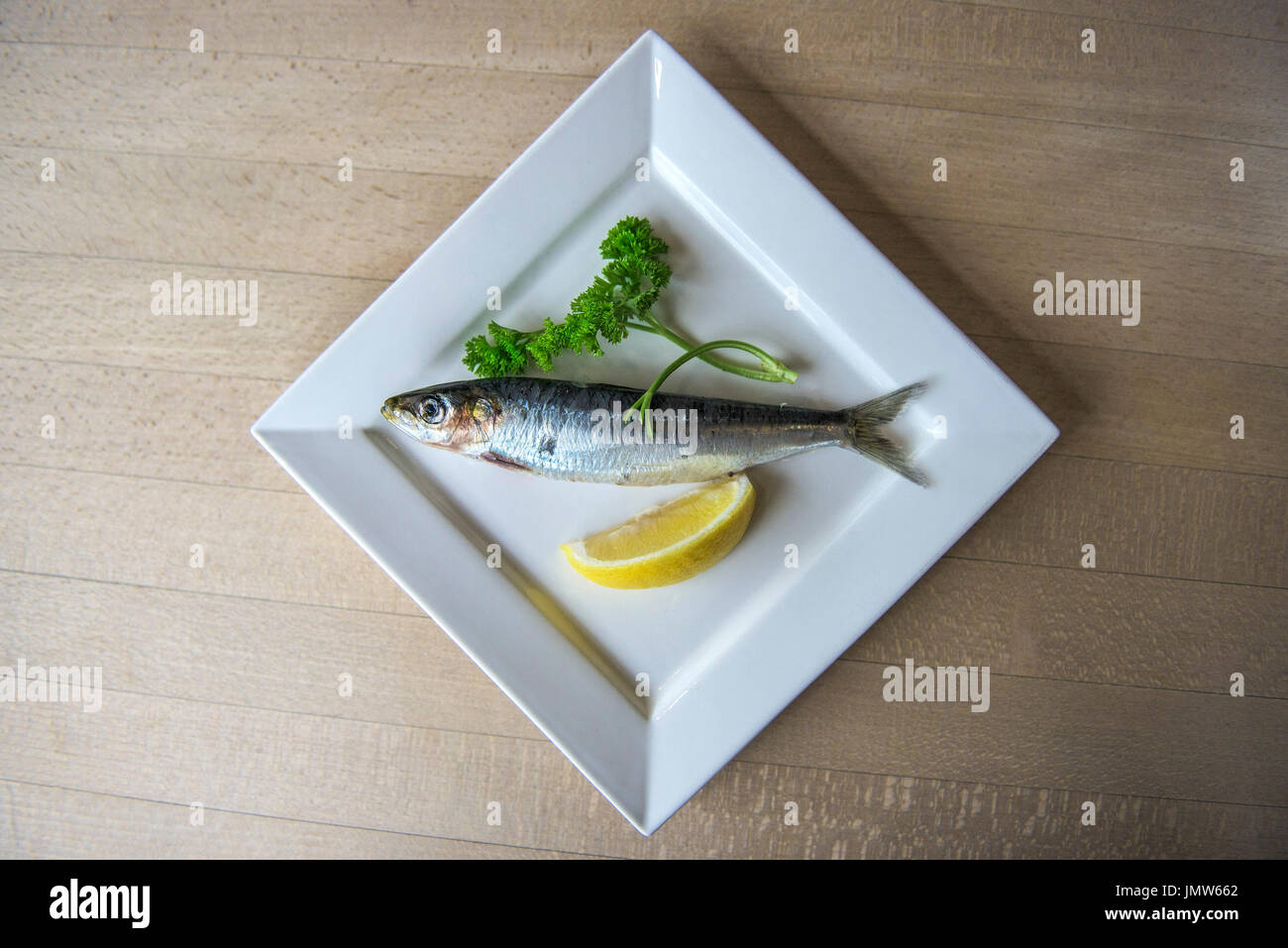 A sardine, sprig of parsley and a wedge of lemon on a plate. Stock Photo