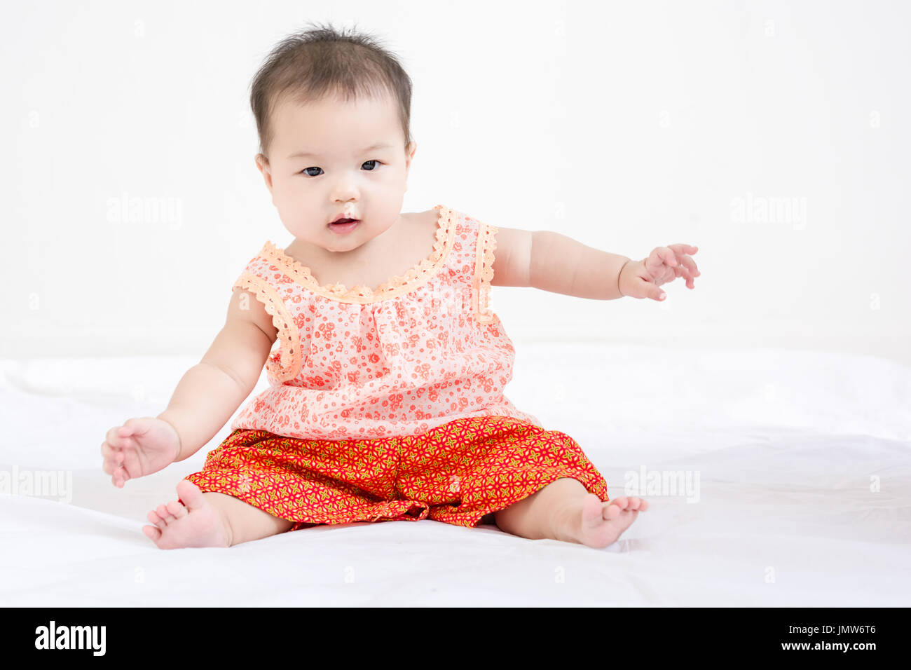 Portrait of a little adorable infant baby girl sitting on the bed and ...