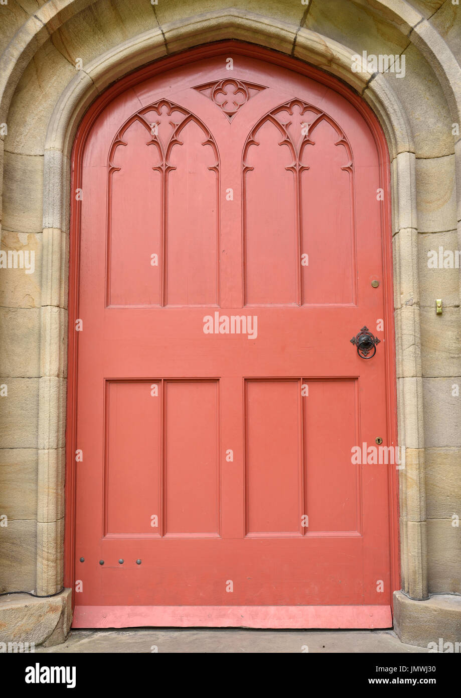 Red Wooden church door in stone surround all saints church stand Stock Photo