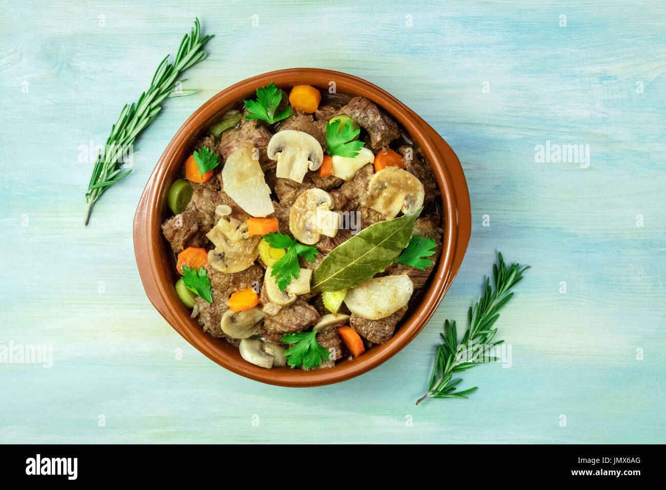 A photo of a meat ragout in an earthenware bowl, with branches of fresh
