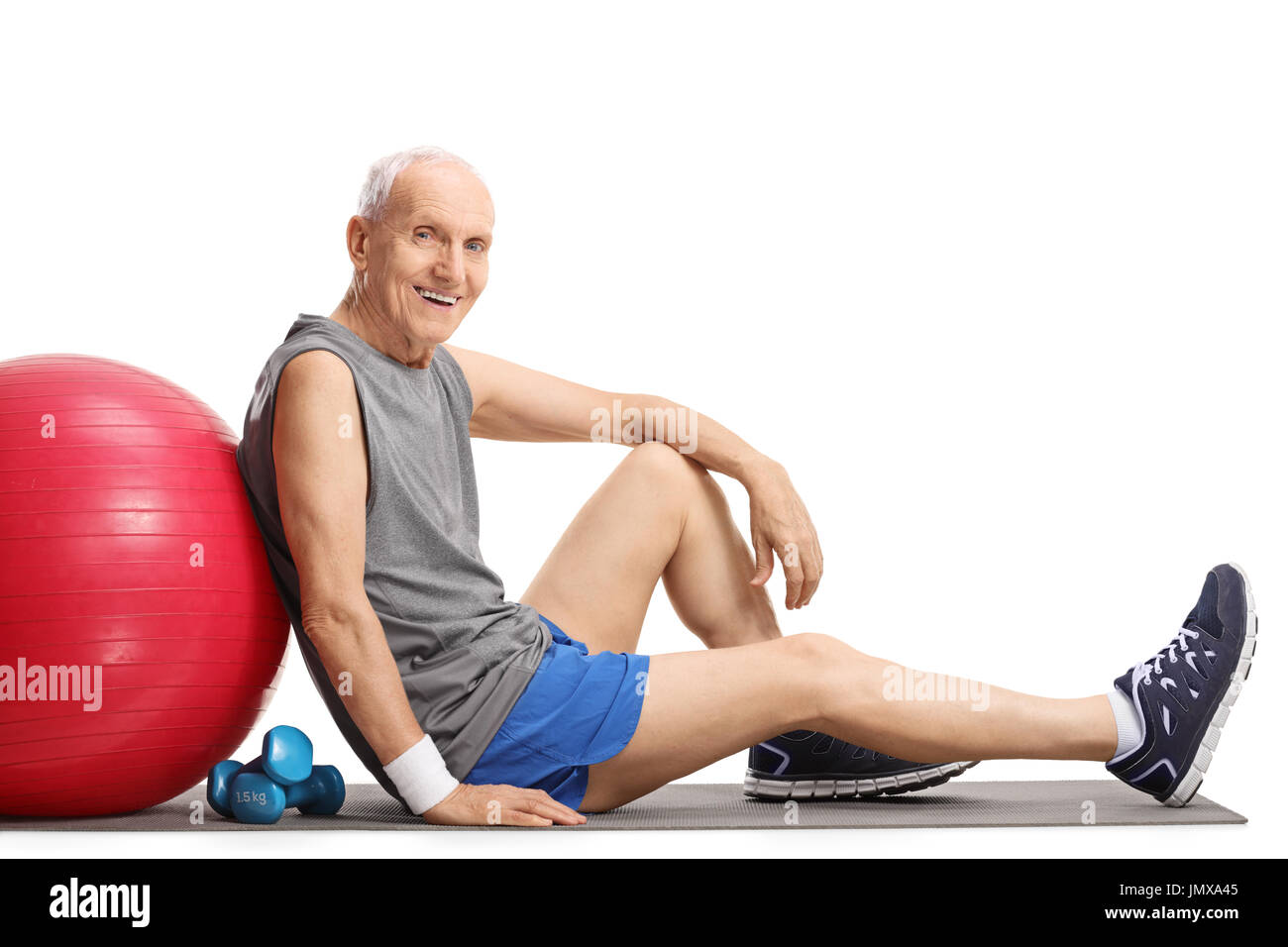 Senior with a pilates ball and dumbbells sitting on an exercise mat isolated on white background Stock Photo
