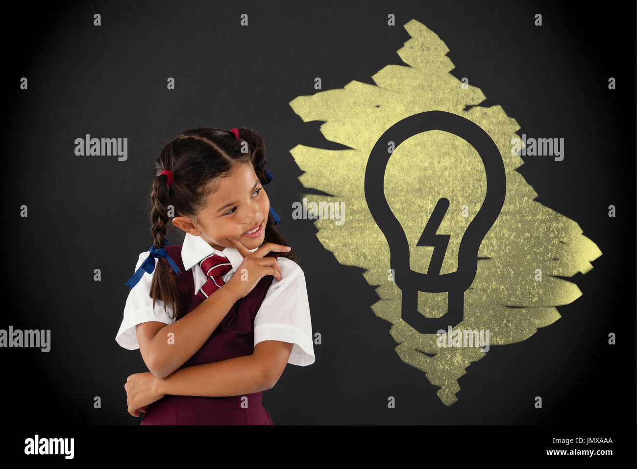 Light bulb on black scribbling against schoolgirl standing against blackboard in classroom Stock Photo