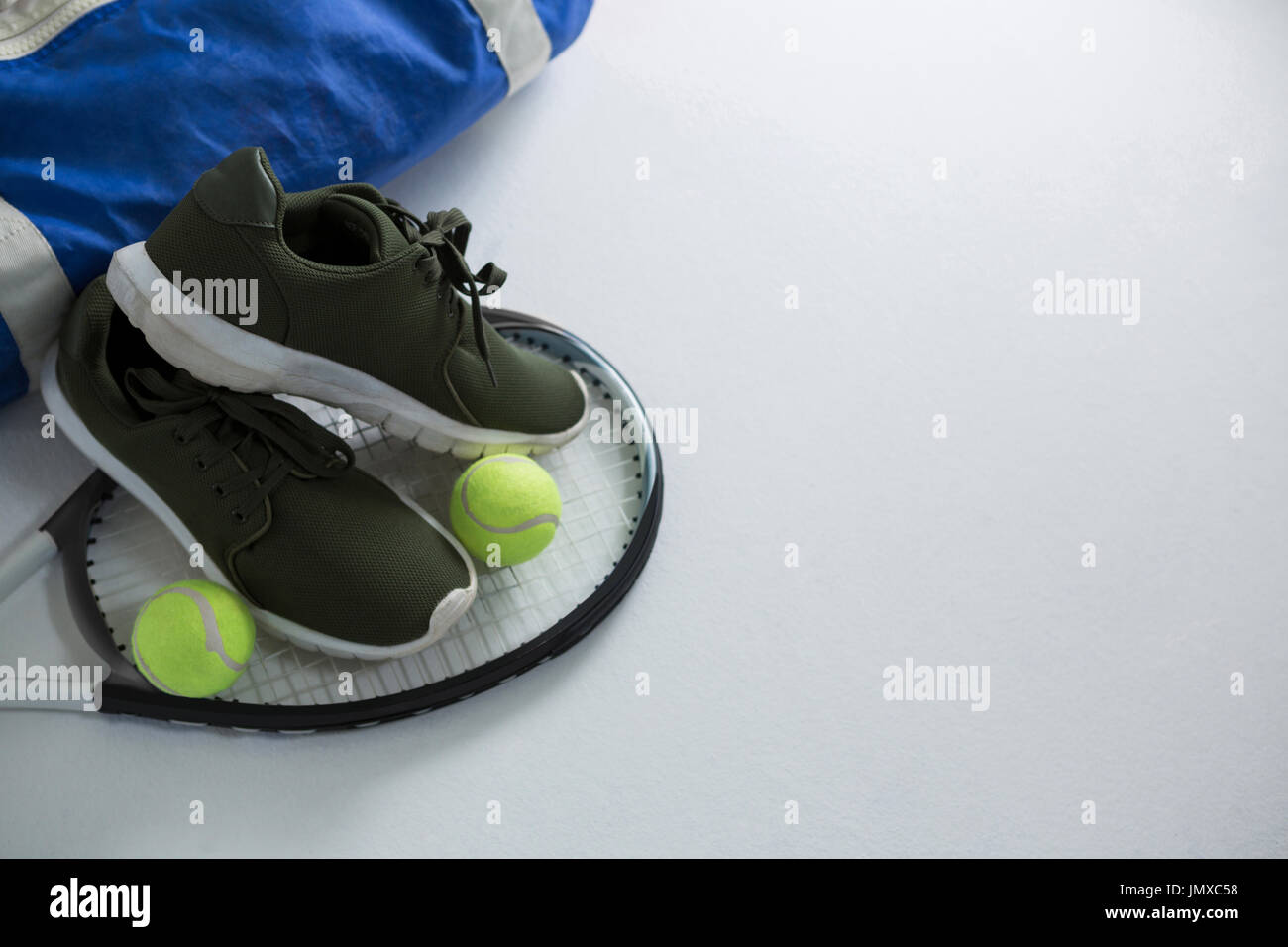 Sports shoe and tennis balls on racket by bag over white background
