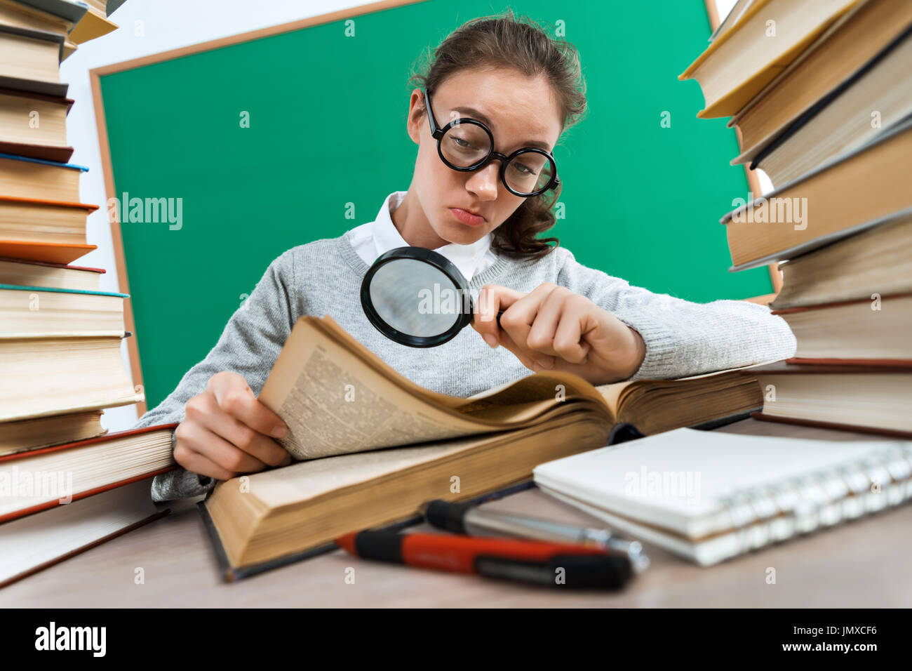 Student with a magnifying glass seeks the answer in book. Photo of girl