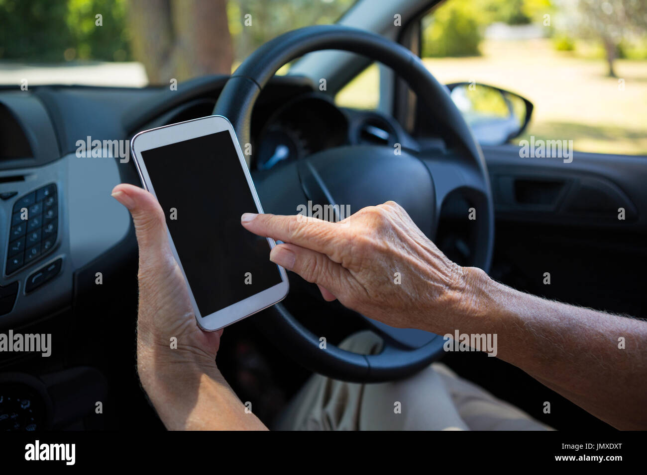 Using Console While Driving Mid-section of senior woman using digital tablet while driving car ...