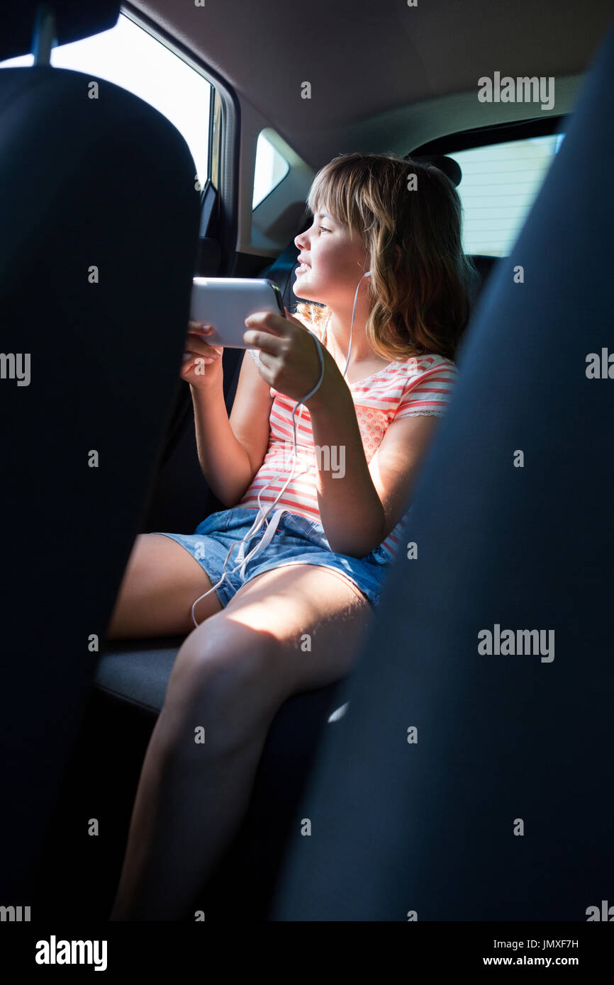 Happy teenage girl in headphones using mobile phone in the back seat of car Stock Photo