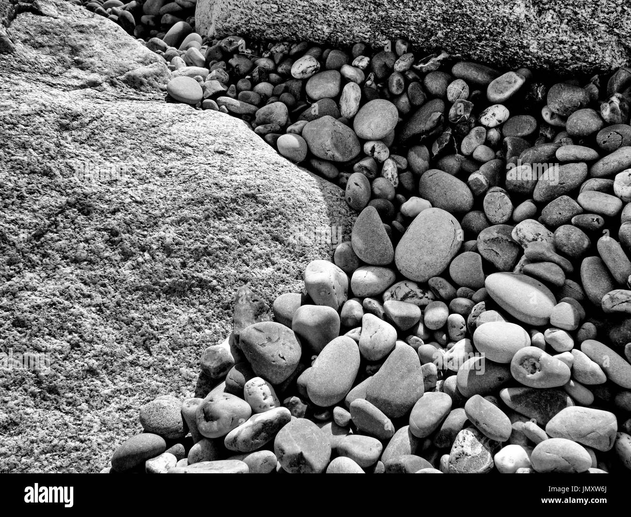 Worn and rounded pebbles forming interesting patterns in the gaps between the rocks of a rock armour groyne on a Devon beach. Stock Photo