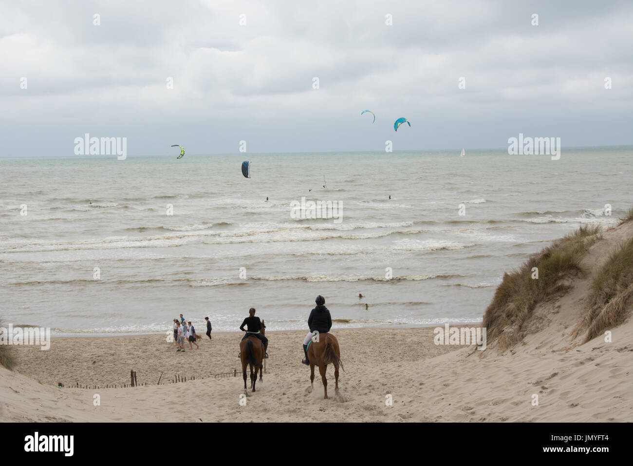 Horse riders make there way to the beach at Le Touquet, France. The windy day is ideal for kite surfers Stock Photo