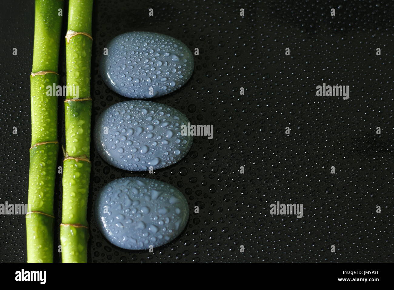 Black background with bamboo branch on the left and gray zen pebbles with drops of water Stock Photo