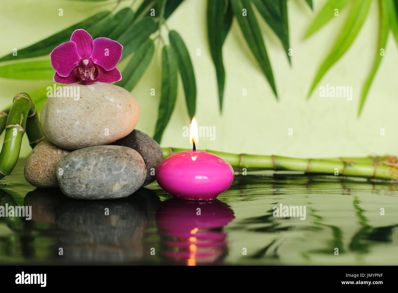 Pebbles laid  on the left out in zen lifestyle with an orchid at the top and a pink candle lit Stock Photo
