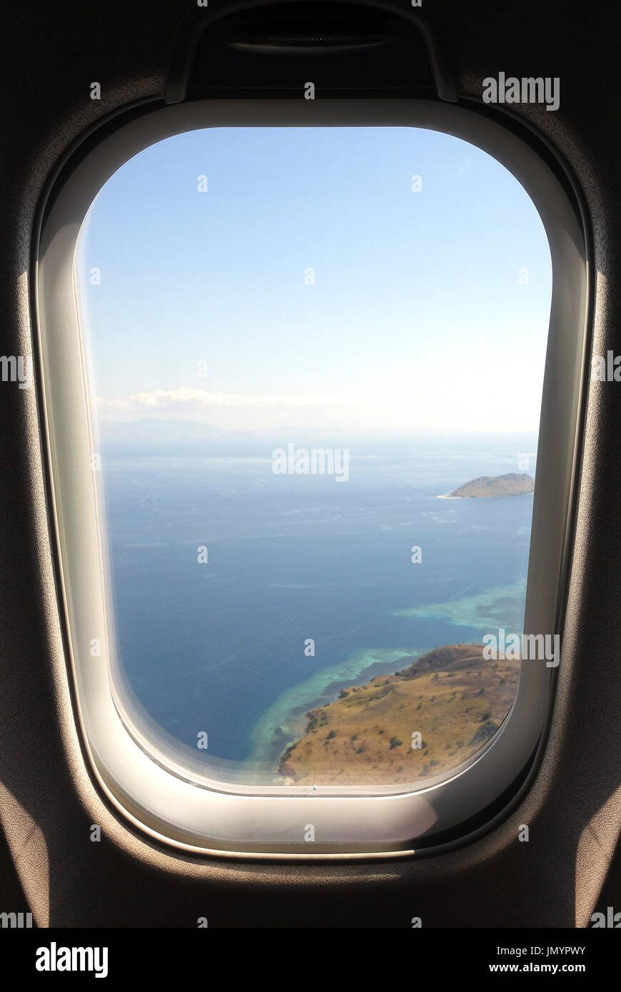 Looking out airplaine window seat at exotic tropical coast of islands and blue turquoise colored ocean water while arriving at Flores, Indonesia Stock Photo
