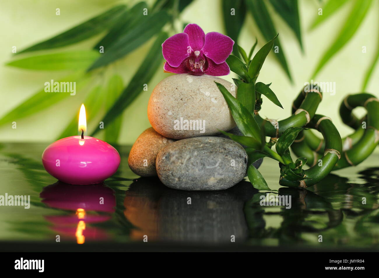 Pebbles arranged in Zen lifestyle in the center with an orchid at the top with bamboo stalks and a lighted pink candle Stock Photo