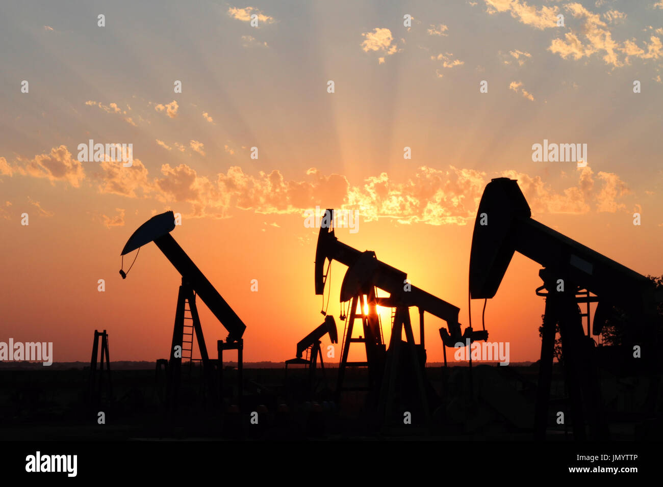 Several oil rigs stand in silhouette with a brilliant sunset in the
