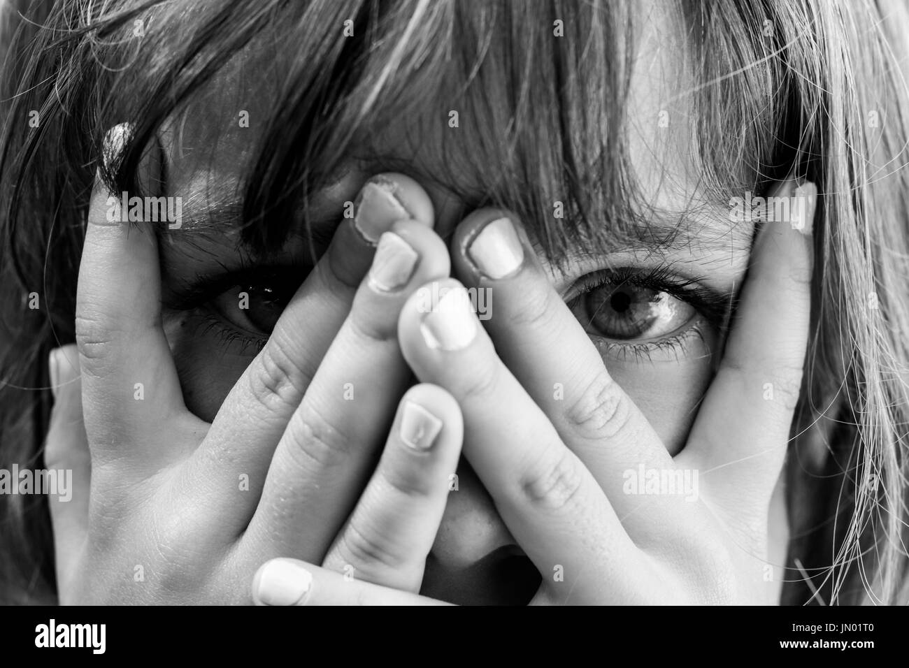 Conceal and reveal: Black and white close up portrait of a young girl hiding behind her hands Stock Photo