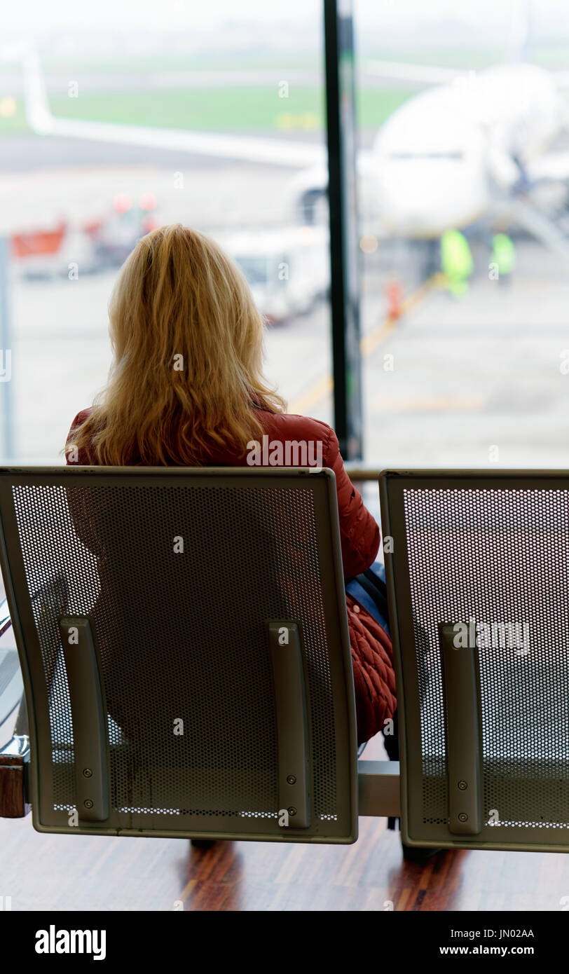 Woman sitting and waiting for her flight in the departure hall of Milan-Bergamo airport in Italy. Airplane on the background Stock Photo
