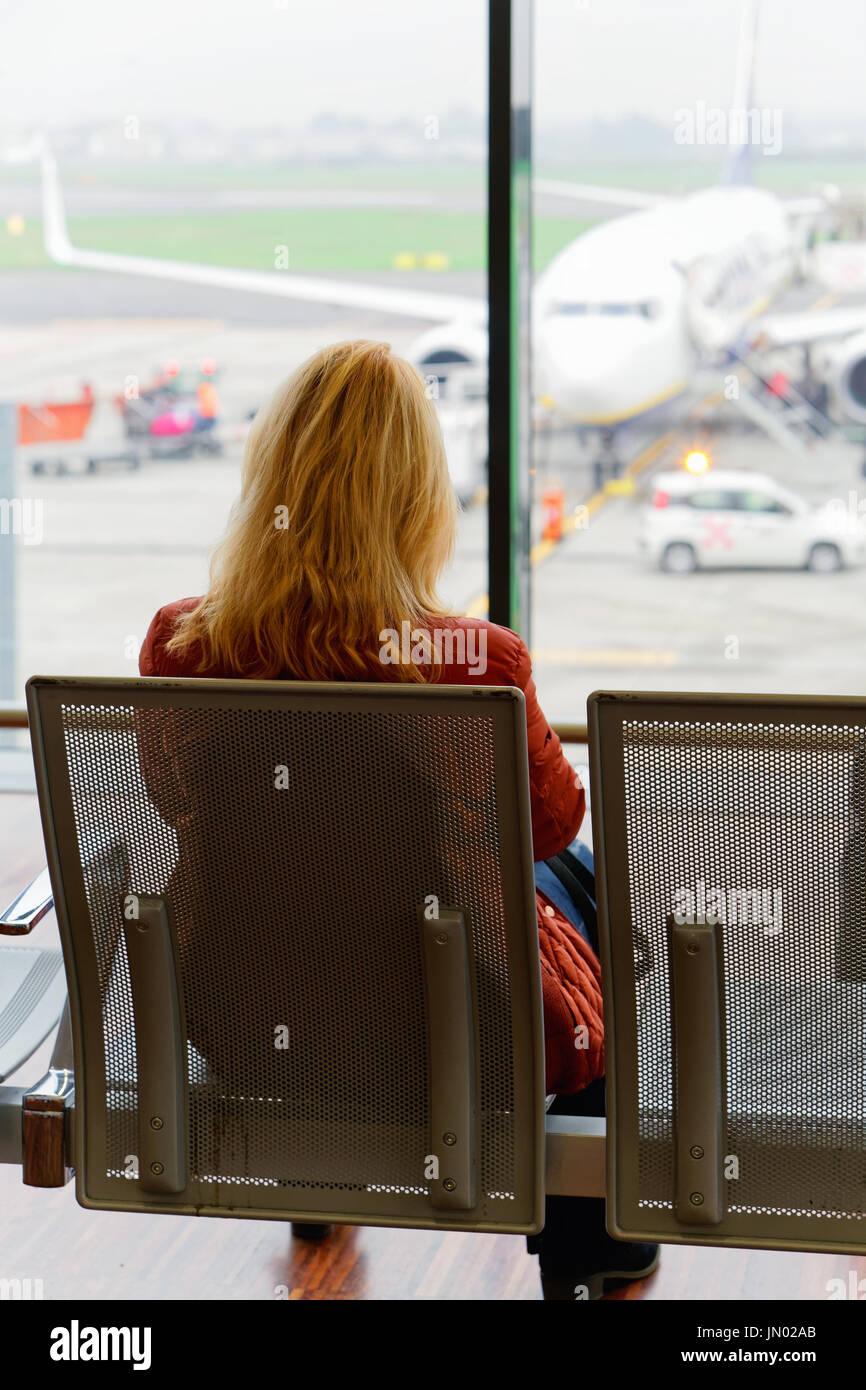 Woman sitting and waiting for her flight in the departure hall of Milan-Bergamo airport, Italy. Airplane on the background Stock Photo