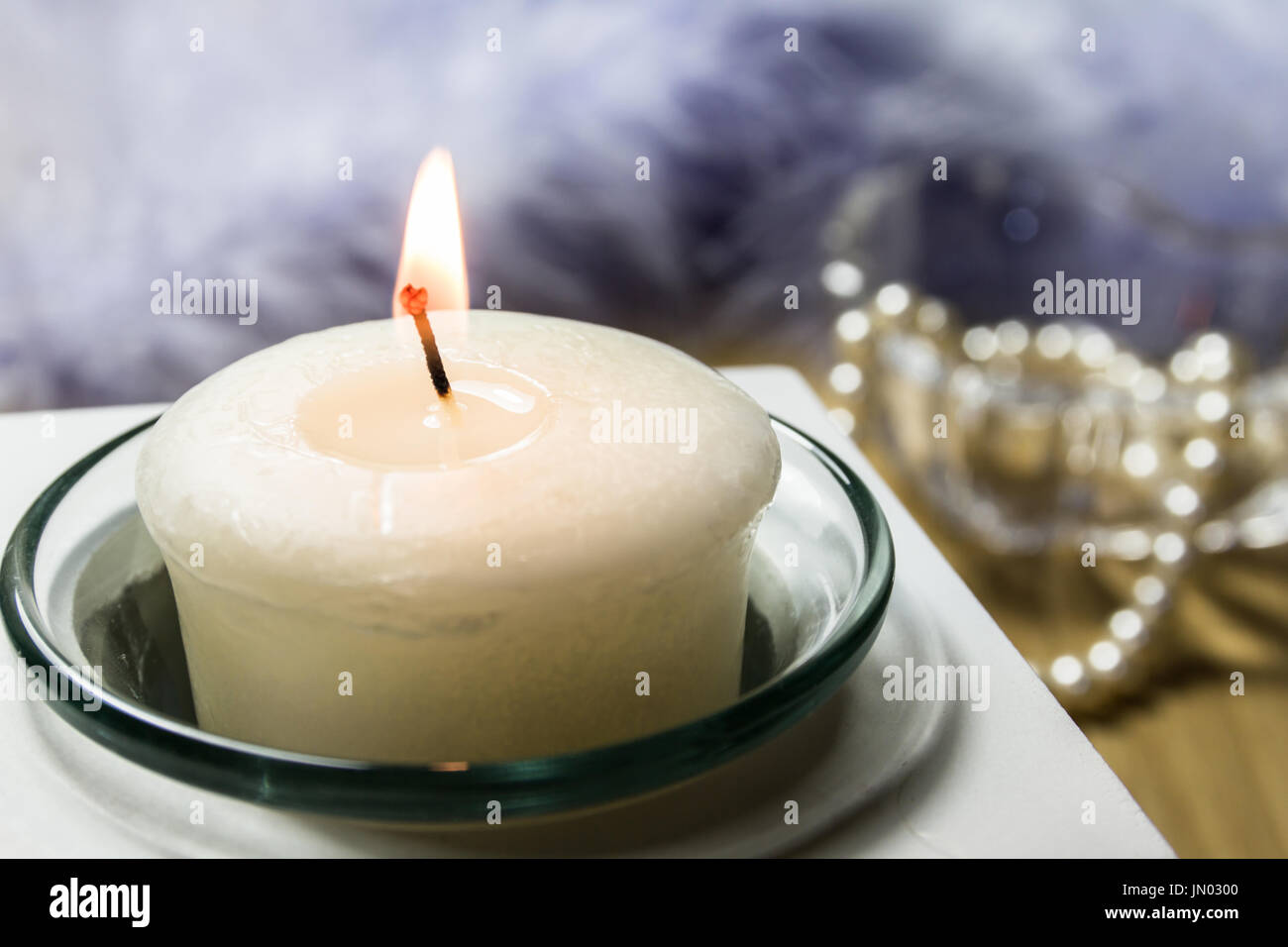 Still Life of a Lighted Candle in a glass container, with pearls in a glass jar, and a Blue Feather Boa blurred out in the background Stock Photo