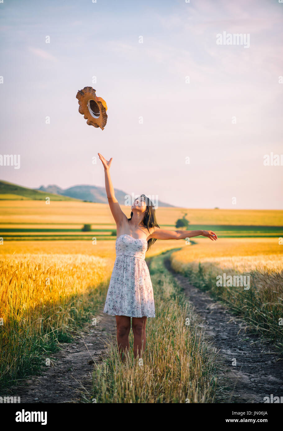 Young happy woman in a wheat field with white dress and summer hat ...