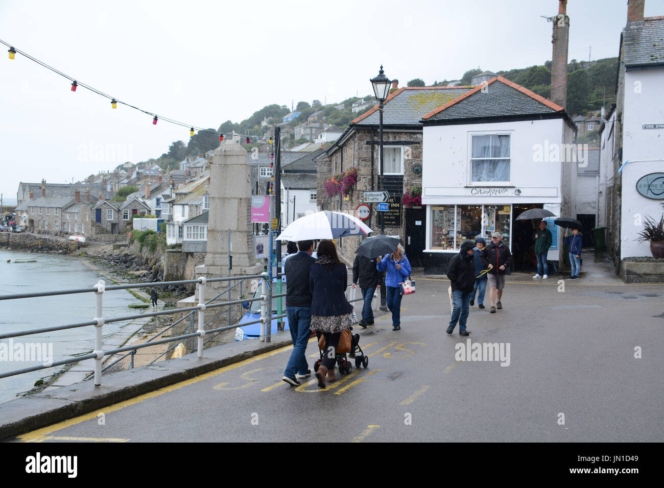 Mousehole, Cornwall, UK. 29th July, 2017. UK Weather.Holiday makers out in the tiny village of Mousehole, with their umbrellas. Credit: cwallpix/Alamy Live News Stock Photo