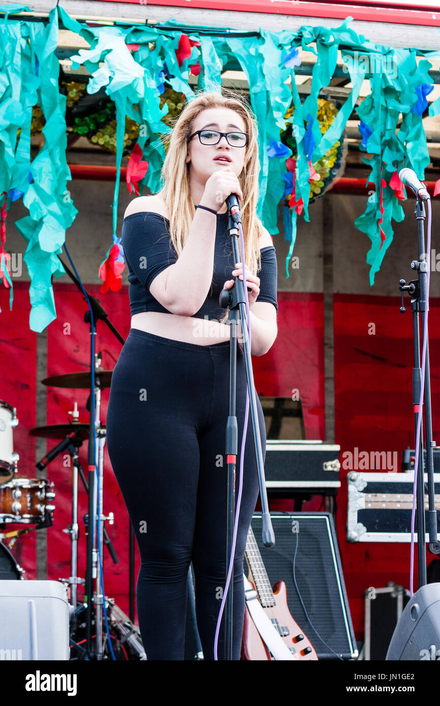 Young Caucasian blonde woman with glasses standing on stage singing. Dannli Jayne, singer song
