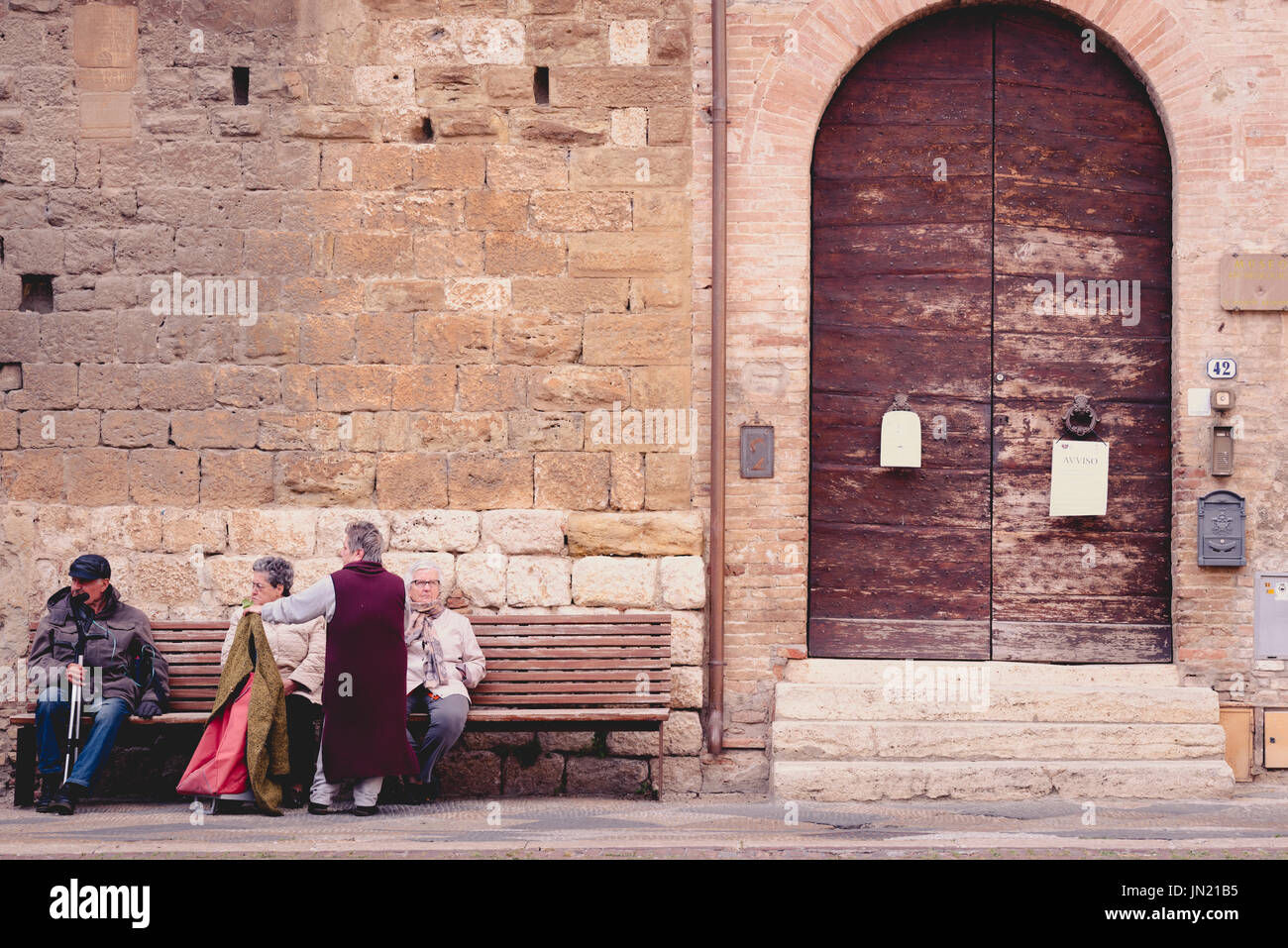 COLLE VAL D'ELSA, ITALY - APRIL 25, 2017 - A group of senior people relax on a public bench in the historic district of Colle Val d'Elsa, a small town Stock Photo