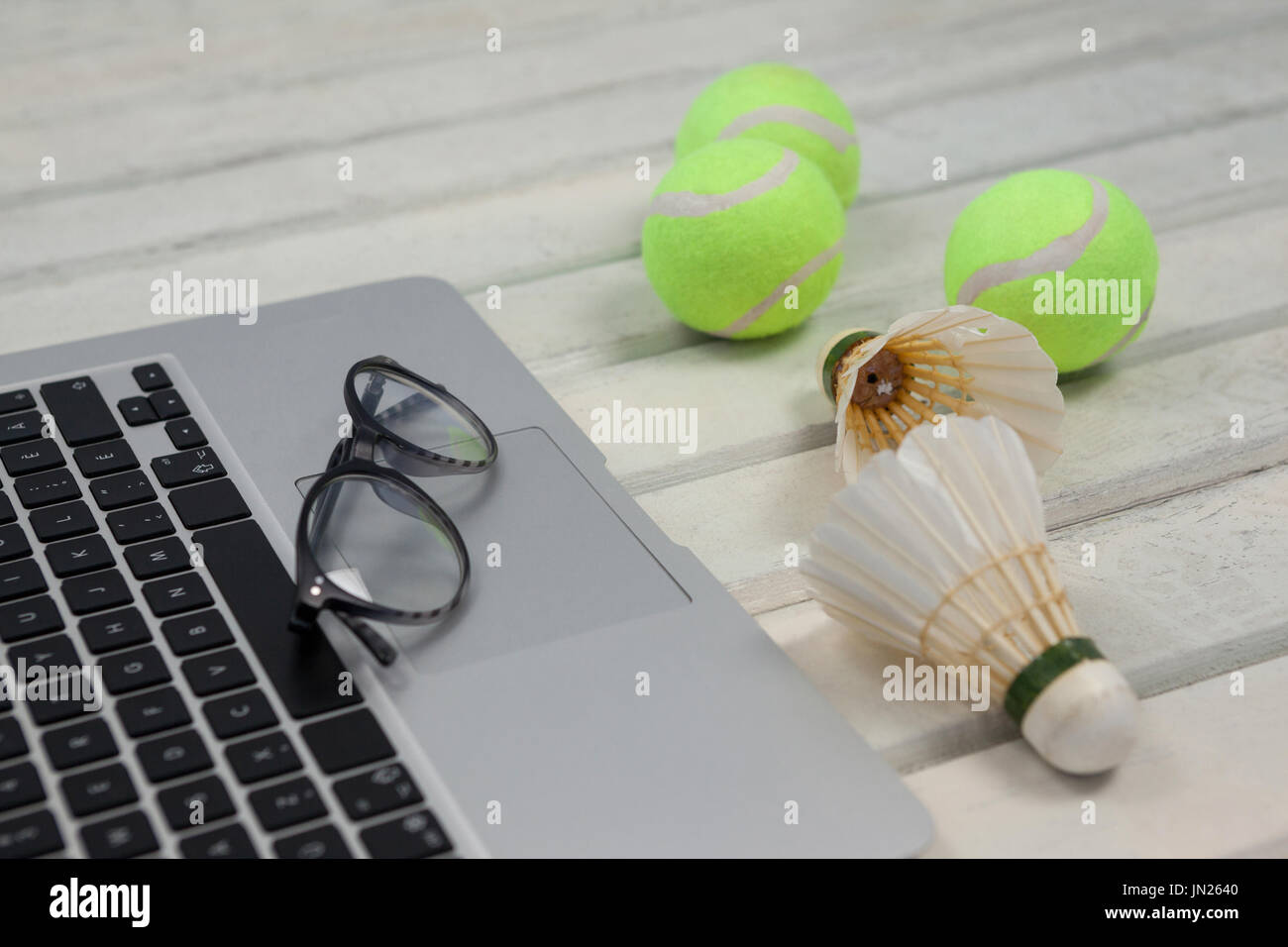 High angle view of eyeglasses on laptop by shuttlecocks and tennis balls on white wooden table Stock Photo