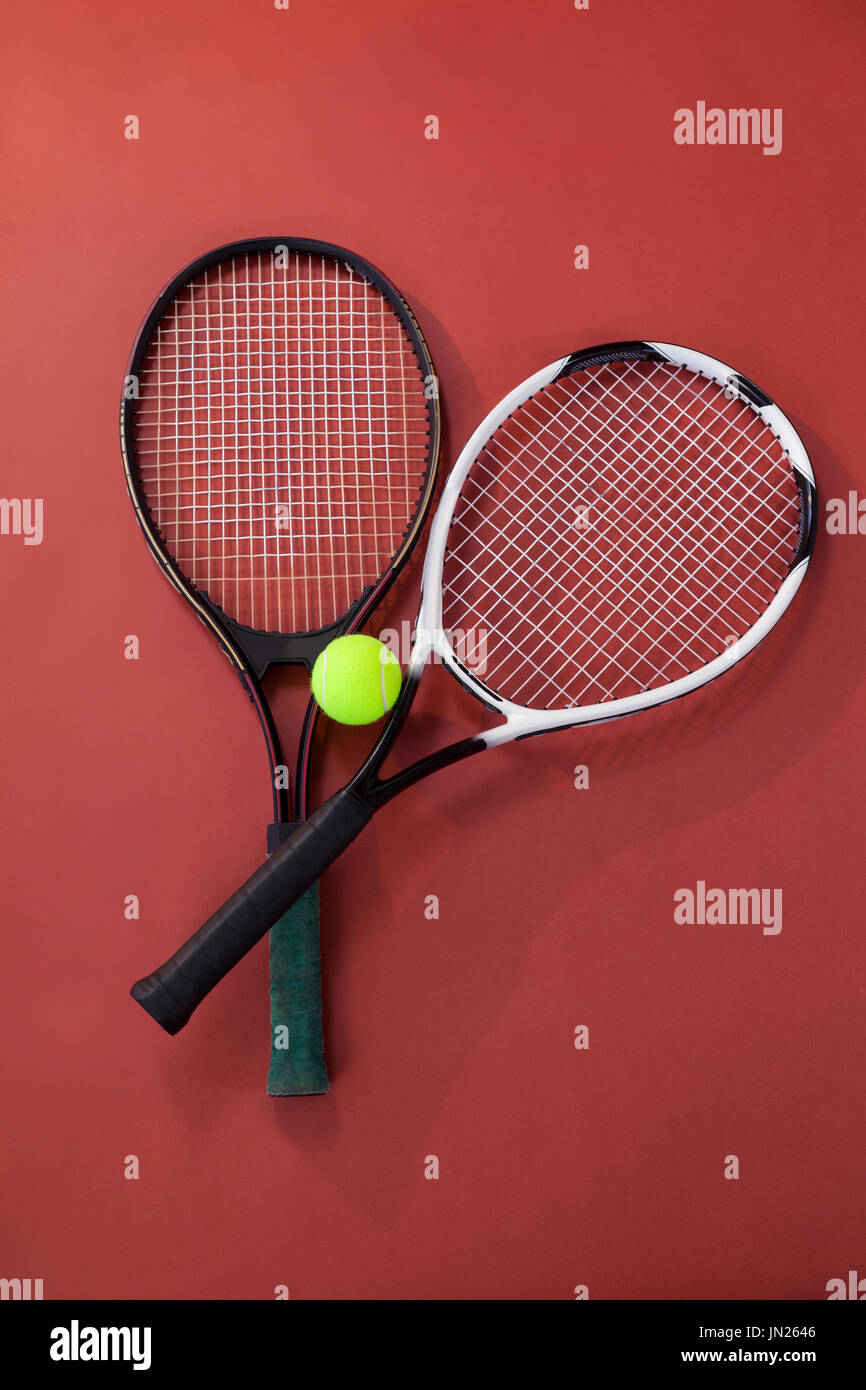 Overhead view of tennis ball amidst rackets on maroon background Stock Photo