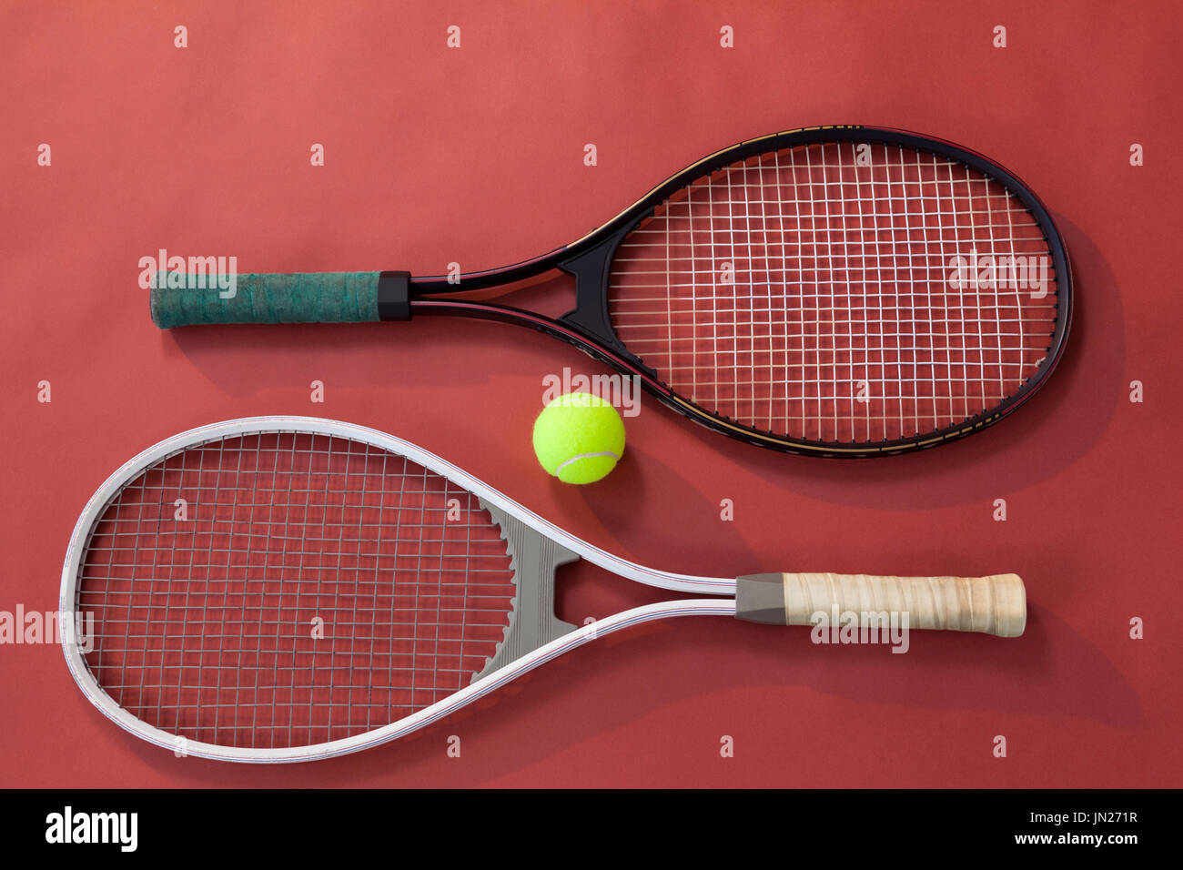 High angle view of ball amidst tennis rackets on maroon background ...