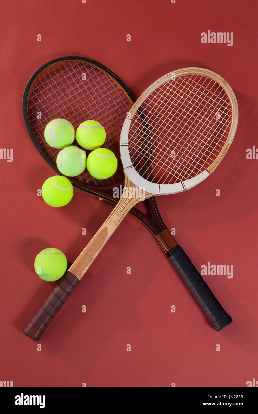 Overhead view of tennis balls with wooden rackets on maroon background Stock Photo
