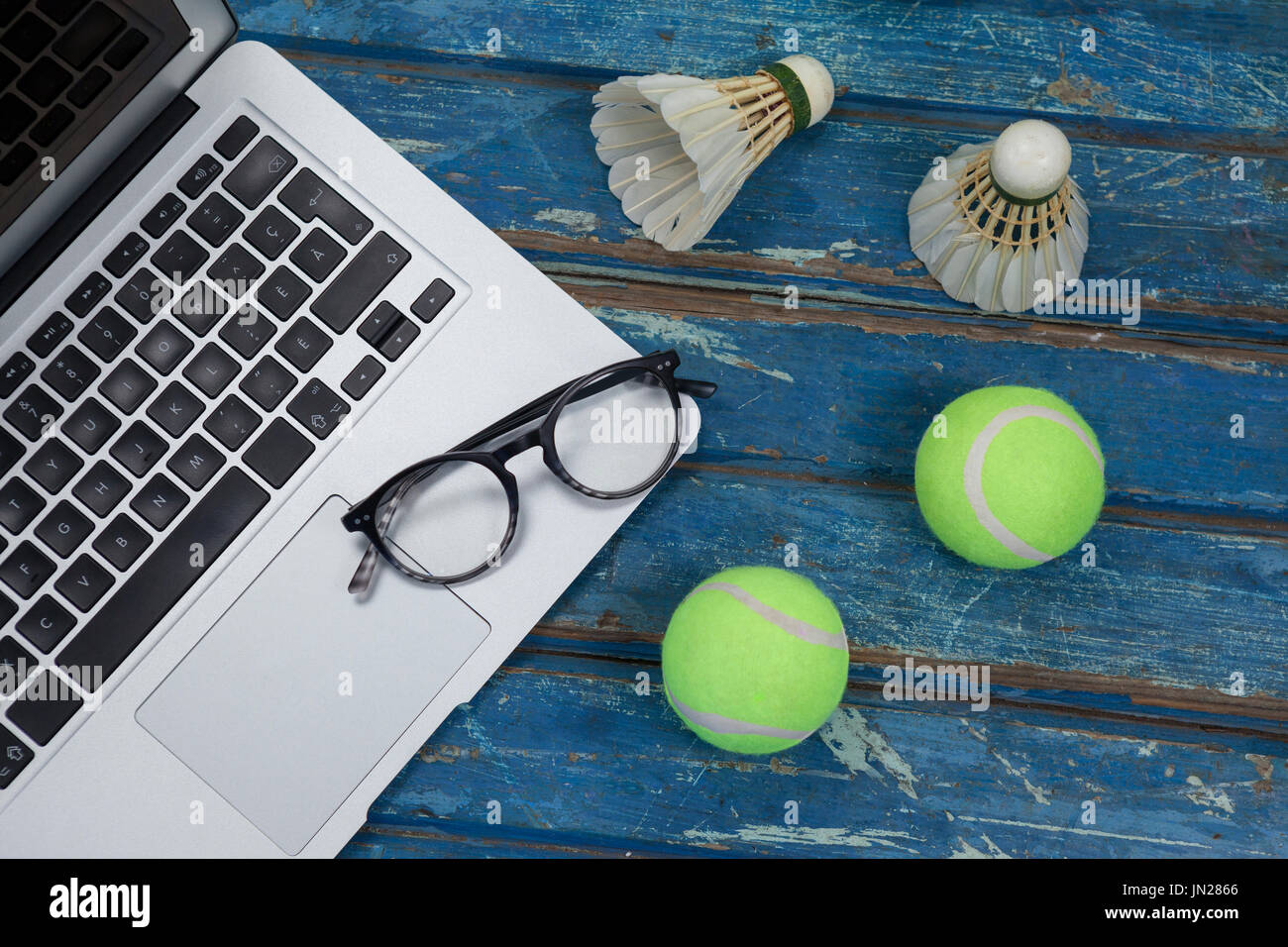 High angle view of laptop and eyeglasses with shuttlecocks by tennis balls on blue wooden table Stock Photo