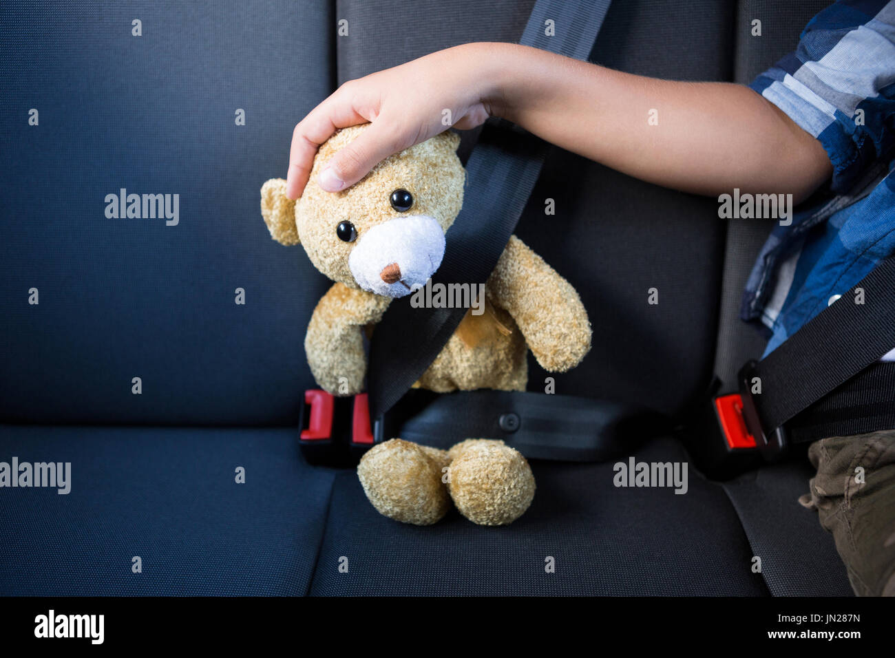 Mid-section of teenage boy sitting with teddy bear in the back seat of ...