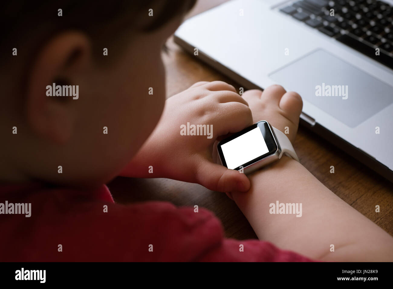 Close up of boy using smart watch by laptop at table Stock Photo
