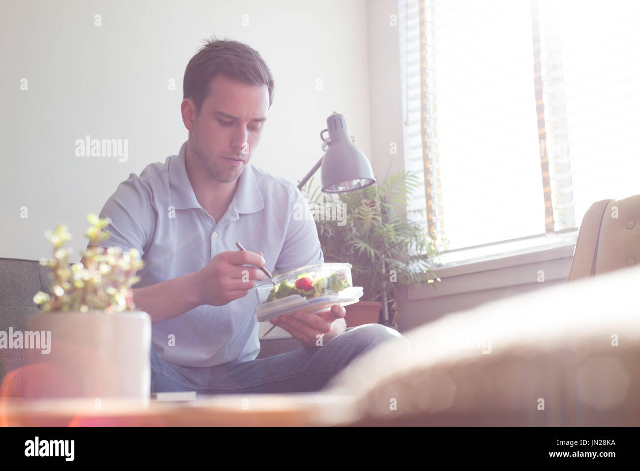 Man having food while sitting on sofa by window at home Stock Photo