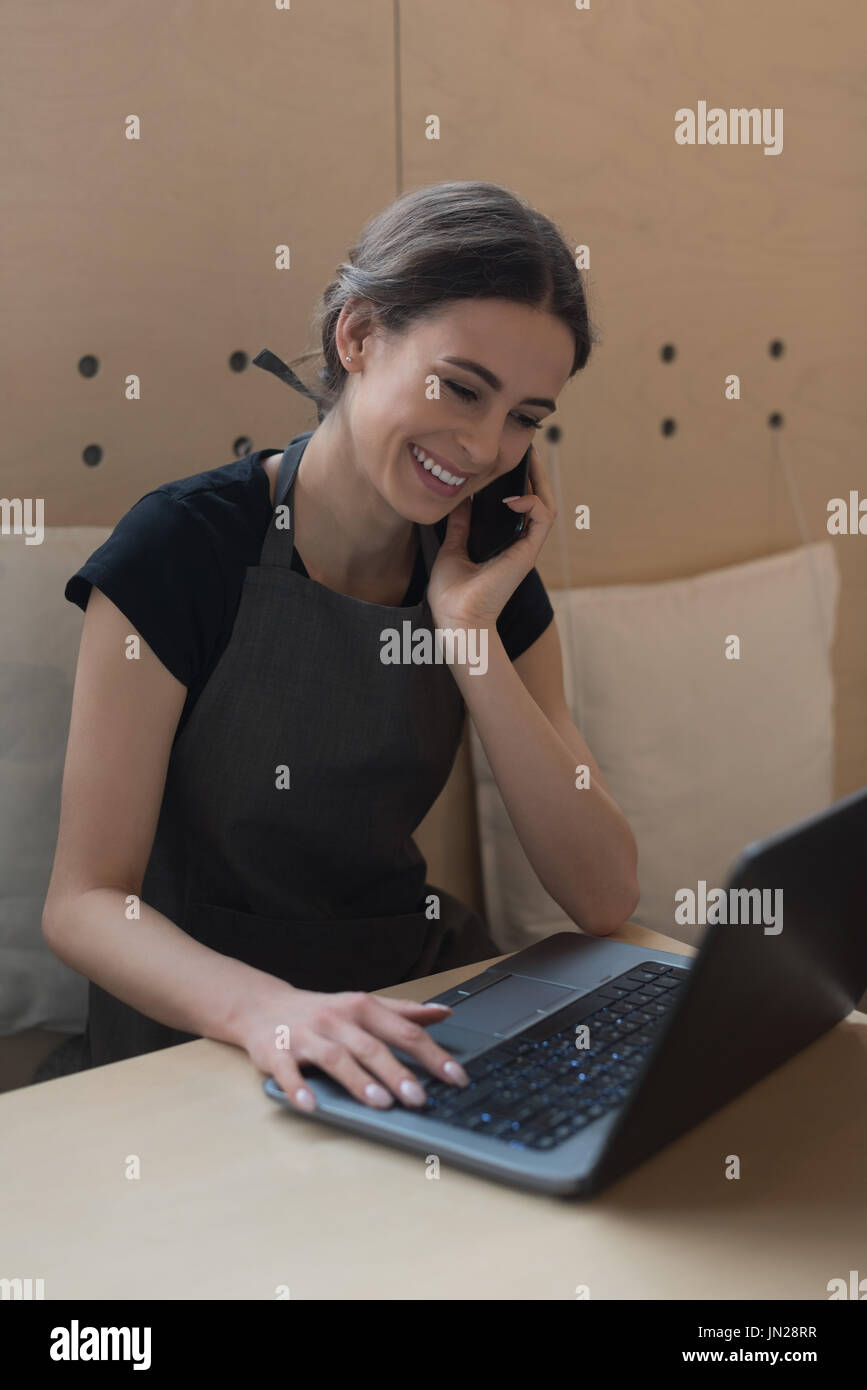 Owner talking on phone while using laptop at table in cafe Stock Photo