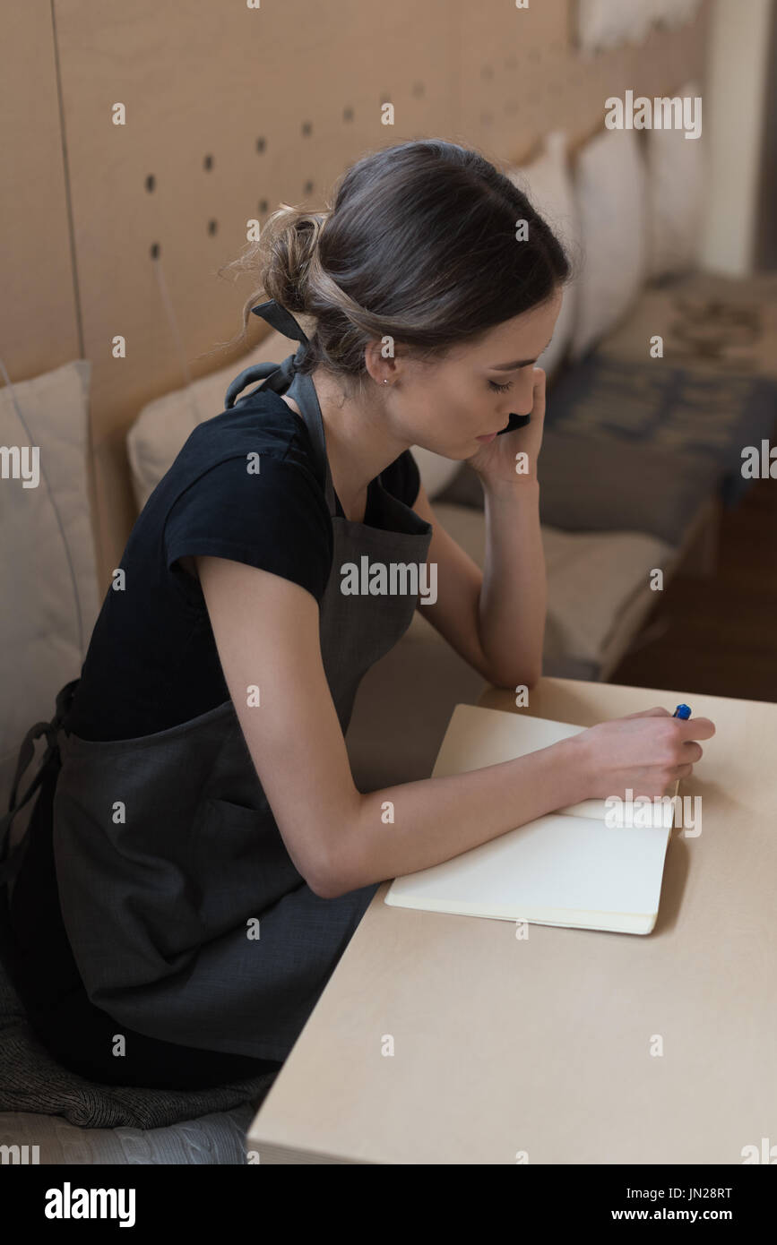 High angle view owner talking on phone while writing on diary at table in cafe Stock Photo