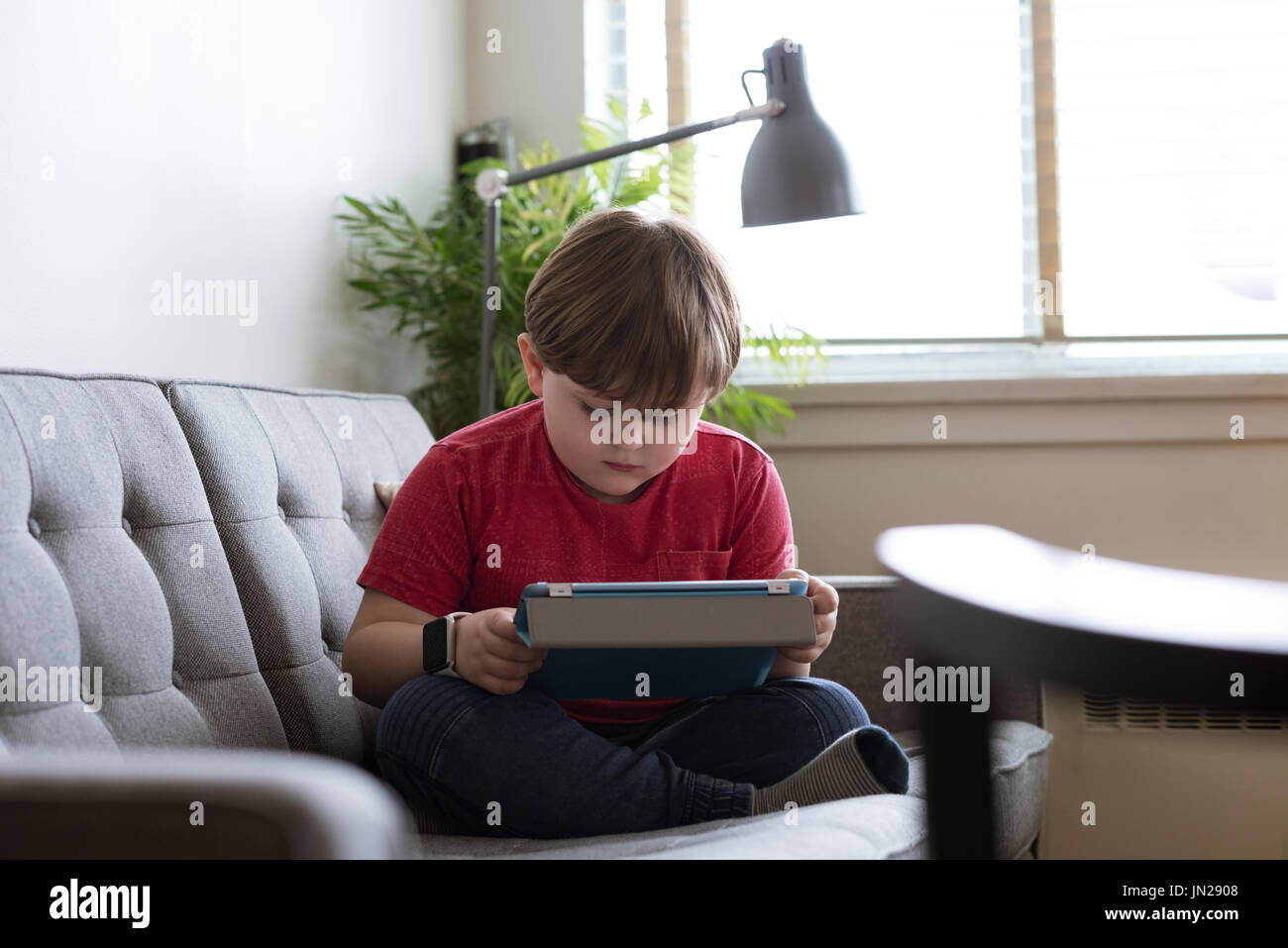 Cute boy using tablet computer while sitting on sofa Stock Photo