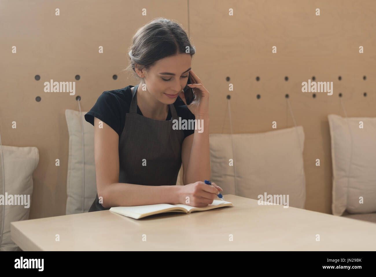 Owner talking on phone while writing on diary at table in cafe Stock Photo