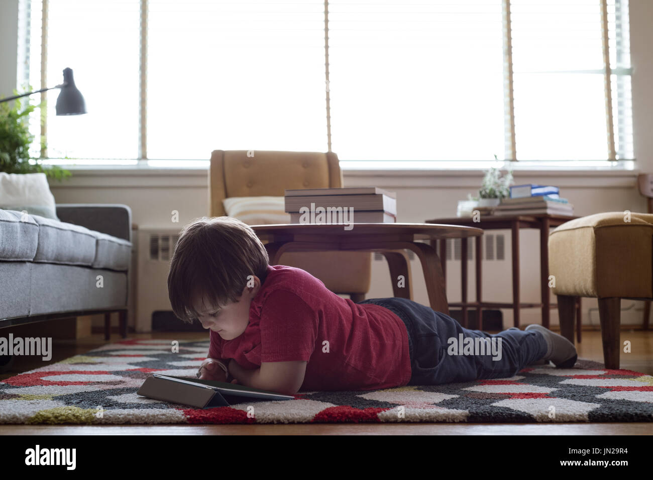 Boy using tablet computer while lying on carpet in living room Stock Photo