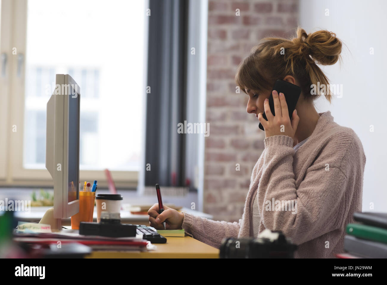 Woman talking on mobile phone while writing sticky notes in cafe Stock Photo