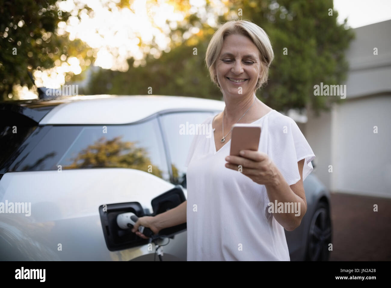 Smiling woman using mobile pone while charging electric car Stock Photo