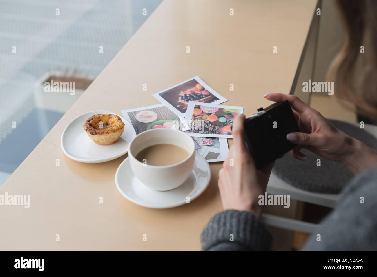 Cropped image of woman photographing coffee by cupcake and photographs on table in cafe Stock Photo