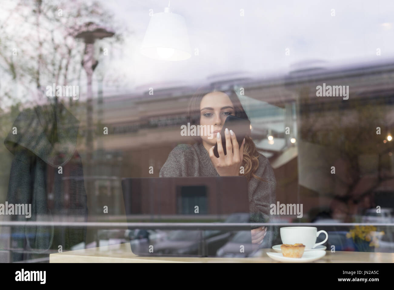 Woman using phone in cafe seen through window Stock Photo