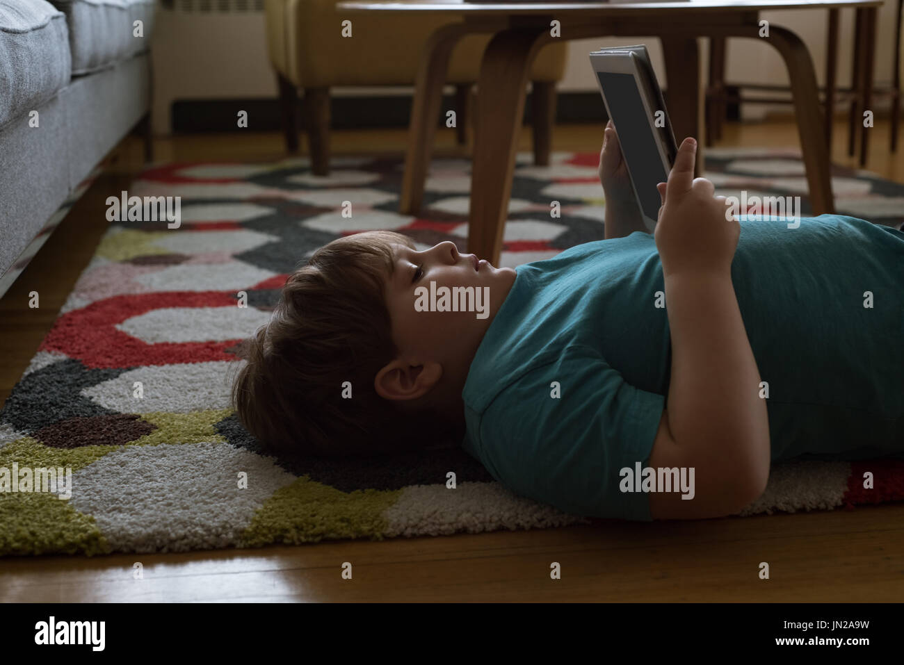 Side view of boy using digital tablet while lying on carpet at home Stock Photo