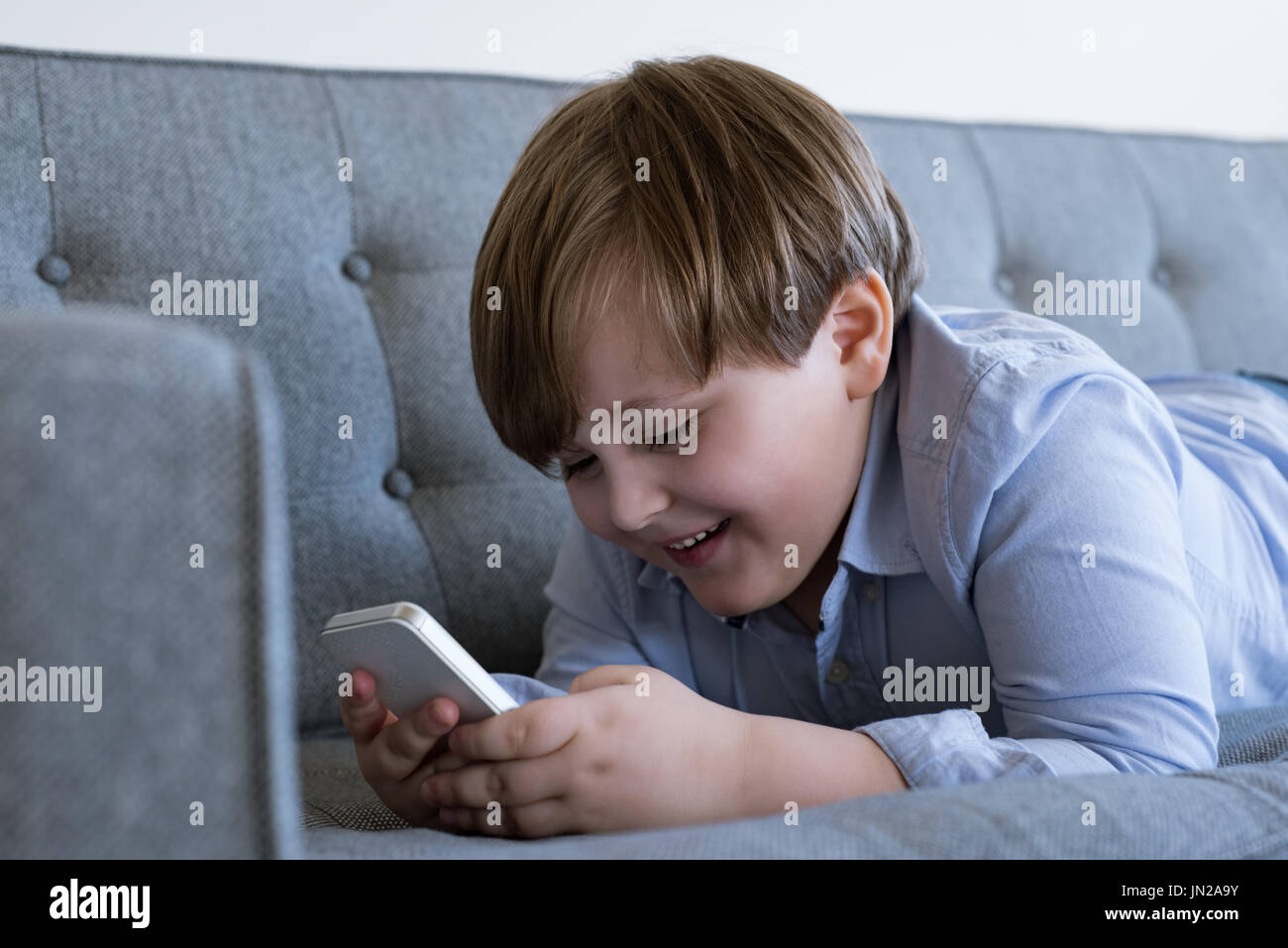 Smiling boy using mobile phone while lying on sofa at home Stock Photo